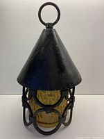 Front view of hand made ceiling light showing wrought iron conical top and ring for hanging, with amber textured glass shade inside a wrought iron frame.