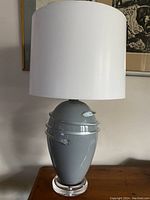 Full view of the lamp off with white lampshade showing grey/blue glass body and lucite base.