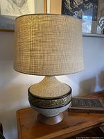 Full view of the mid-century textured lamp on a wooden surface with burlap shade and teak base.