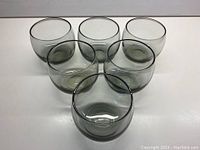 Six smoky grey Mid-Century Modern Roly Poly Scotch glasses arranged on a white surface, showing their rounded shape and size.