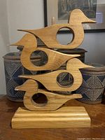Front view showing four light wood birds in silhouette stacked vertically with circular cutouts on a rectangular wooden base.