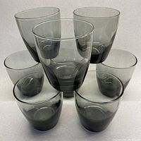 Seven of the eight smoky grey lowball glasses arranged with one glass centered in front and six arranged behind it.