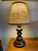 Front view of the lamp lit, showing burlap shade glowing warmly and wooden turned base