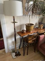 Full view of the West Elm chrome floor lamp standing next to a wooden console table and chair, shows the round lampshade on the lamp.