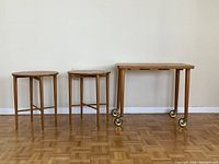 Front and side view of the three wooden tables: one rectangular table on casters and two round stools.