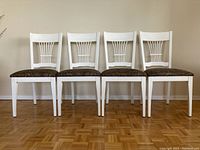 Four white painted wood kitchen chairs with upholstered brown fabric seats arranged side by side showing front view.
