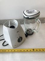 Braun blender base and glass jug with lid separated, placed on countertop with measuring tape showing dimensions.