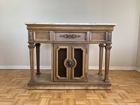 Front view of wood console table with marble top and decorative details on legs and cabinet door.