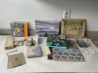 Photo showing collection of assorted gift items including puzzles, candles, stationery, gift bags, and linens on a white surface.