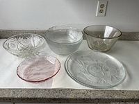 Overall view of all five glass bowls and plates arranged on a countertop, showing different sizes and designs.