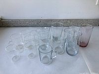Photo showing a collection of 14 clear and tinted drinking glasses of various sizes and styles placed on a granite countertop.