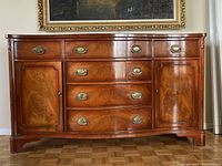 Full frontal photo of a mahogany wood buffet with brass handles and multiple drawers and cabinet doors.