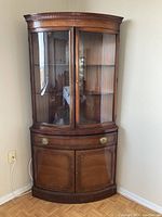 Front view of the mahogany corner cabinet showing glass doors, drawer, and lower wood doors.