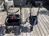 Photo showing front view of two mobility aids on wooden deck: black four-wheel walker with padded arm rests and a blue rollator walker with seat and hand brakes.
