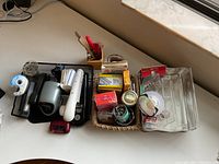 Photo showing assorted office supplies including staplers, tape dispensers, scissors, boxes of staples and pins, pens, and plastic desk organizers arranged on a desk.
