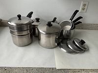 Photo of stainless steel pot set including large stockpot with steamer insert, saucepan with lid, smaller saucepan, and three small saucepans with handles.