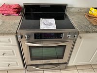 Front view of stainless steel electric range installed between cabinets, showing cooktop and oven door