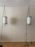 Wide shot showing two identical vintage hanging lamps suspended side by side on metal chains against a white wall.