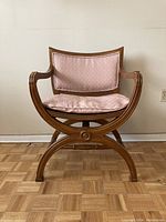 Front view of the wooden chair showing curved X-shaped legs and pink cushioned seat and backrest.