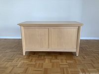 Closed view of the wooden blanket chest showing front panel and legs.