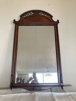 Full front view of vintage wood framed mirror showing its rectangular shape, clear glass, and decorative carved arched top with lattice design.