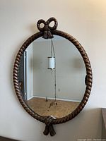 Front view of oval wood-framed mirror with rope design and bow accents