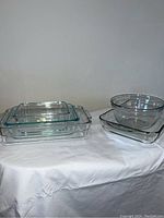 View of five assorted Pyrex clear glass baking dishes on white fabric background showing different shapes and sizes.