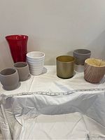 Seven assorted vases arranged on a white cloth against a plain wall, showing color, shapes, and materials.