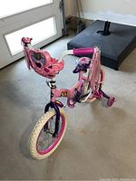 Side angle view of the pink and purple children's bike with training wheels and Disney Princess decorations.