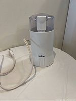 Side view showing the Salton branded electric coffee grinder with white body, clear lid, and attached power cord.