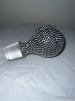 Side view of crystal bottle stopper showing rhinestone encrusted spherical top and frosted glass stopper.