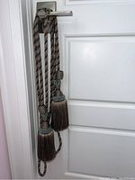 Full view of two curtain tie backs hanging on a door handle, showing braided cords and tassels.