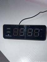Front view of black Marathon digital alarm clock showing LED display and two USB ports on front panel.