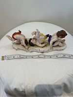 Top view of the porcelain figurine showing three babies on decorative base with measuring tape for size context.
