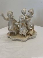 Porcelain figurine of three children in winter attire playing, shown from front view.
