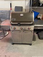 Front view of Weber stainless steel gas barbecue grill with lid down, showing control knobs and base cabinet closed.