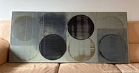 Front view of the acrylic painting showing abstract circular forms in grey and black tones on canvas, resting on a tan leather couch.