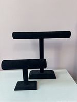 Two black jewelry stands, one taller for necklaces and one shorter for bracelets, both on rectangular bases.