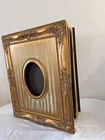 Full view of large ornate gold-tone photo album with embossed floral details and oval photo window on front cover.