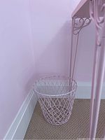 Pink wired metal waste bin placed on carpeted floor in corner against pinkish walls