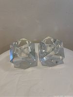 Solid crystal hexagonal shaped candle holders with faceted edges placed on a white surface against a beige wall.