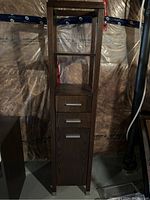 Front view of dark brown wood grain shelving unit showing open top shelves, 3 drawers with metallic handles, and cabinet door below.