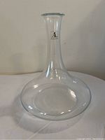 Clear handmade glass wine decanter with label on neck, shown from side on white background.