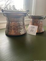 Two antique Turkish copper pots with embossed floral patterns and curved handles on a green surface near a window