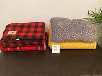 Lot of three folded blankets and throws stacked together against a neutral background with a plant visible on the side.