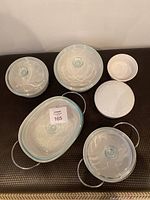 Top view showing six casserole dishes with clear glass lids, one has a metal holder, others are plain white ceramic with ribbed design