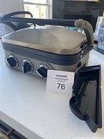 Side angle view of the closed Cuisinart Grill-Panini showing the handle, exterior surface, and control knobs on the front.