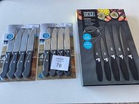 Photo showing two unopened 4-piece Farberware steak knife sets and one unopened Taylor's Eye Witness Brooklyn Kitchen Knife Set still in original packaging on white surface.