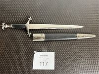 Dagger with metal crossguard and pommel featuring fleur-de-lis, polished steel blade, black handle, and matching black sheath with metal accents.