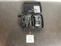 Photo shows a compact black drone with foldable arms, black remote controller, and accessories inside a black zippered carrying case placed on a dark textured surface.